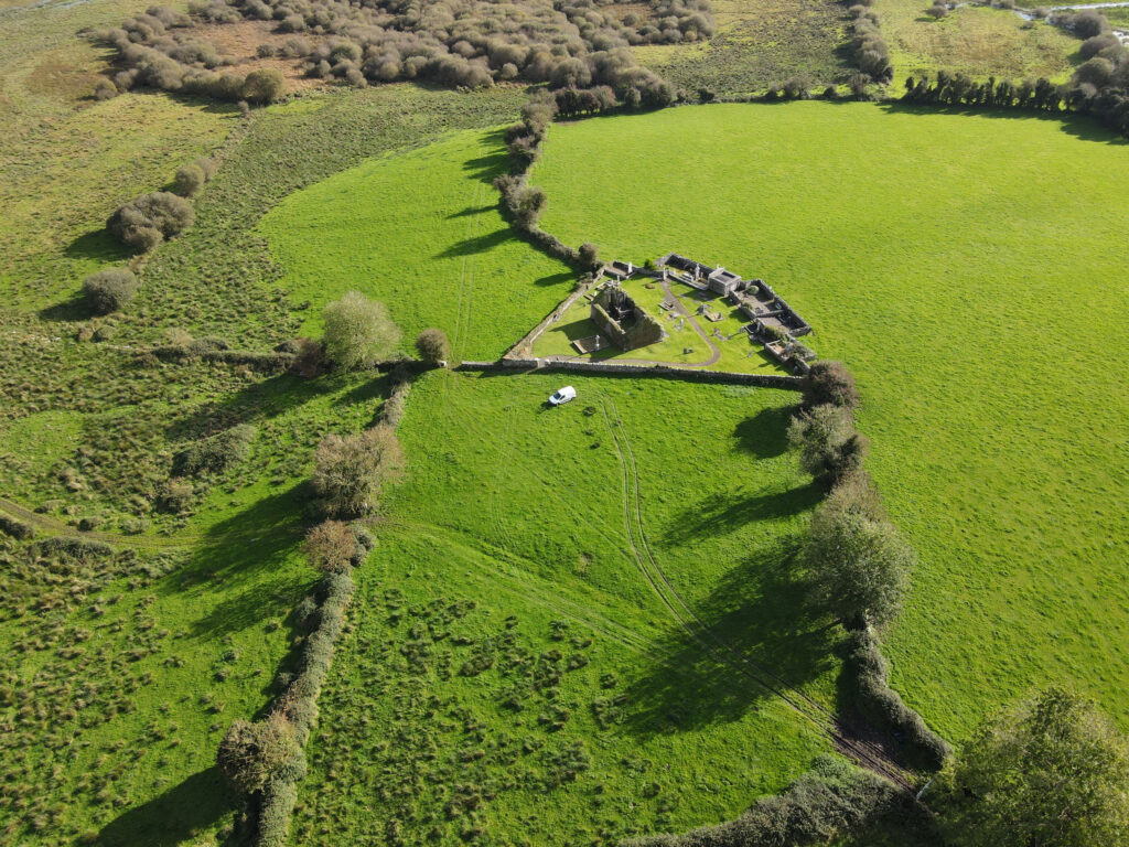 Aerial view of Killoo church and scattered graves, surrounded by grass fields and trees, with a white van parked outside.