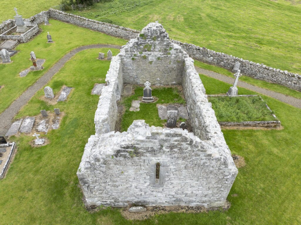 Ruined stone chapel walls surrounded by grassy graveyard with various old tombstones and stone crosses.